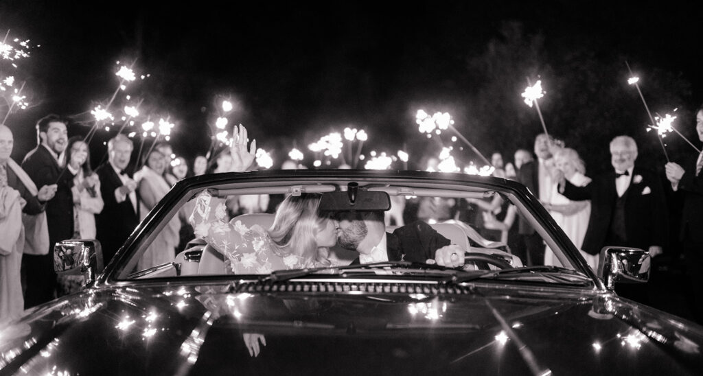 bride and groom sit in vintage car surrounded by vintage cars