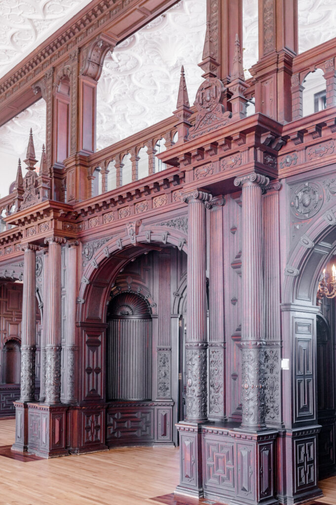 ornate interior of Branford House in CT, featuring intricate woodwork, Gothic-style arches, detailed carvings, and a polished wooden floor with grand architectural elements.