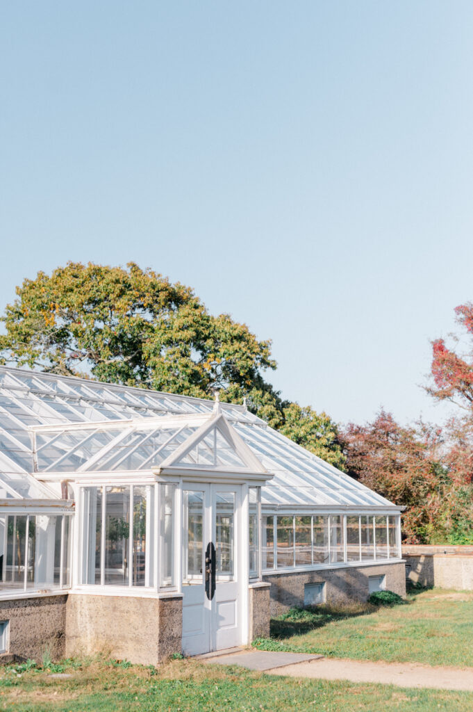 The greenhouse at Eolia Mansion surrounded by lush greenery and trees, under a clear blue sky.