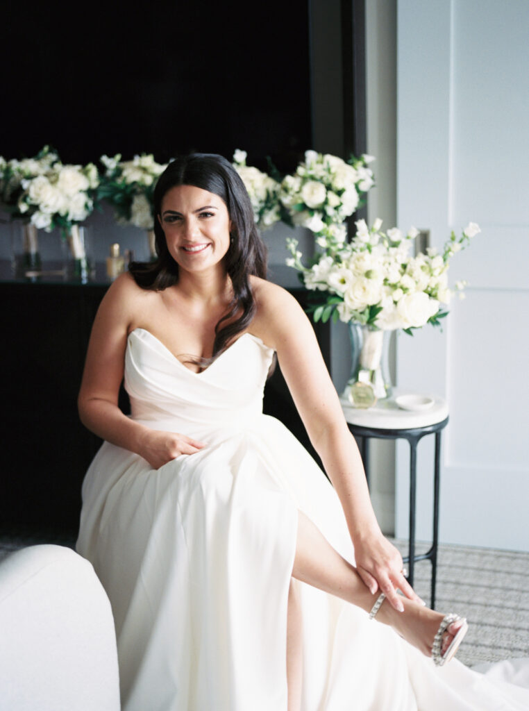 Film photo of bride getting ready, clasping the anklet of her pearl heels. 