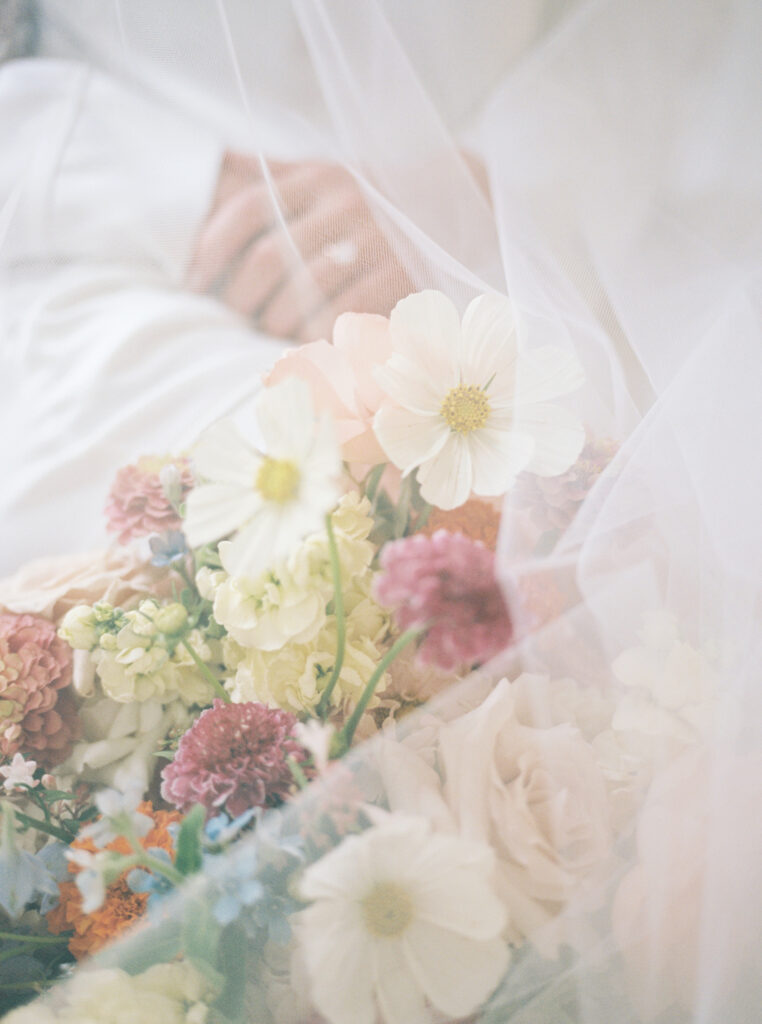 A close-up shot of wedding flowers, covered by a bride’s veil, showcasing the ethereal quality of film photography.