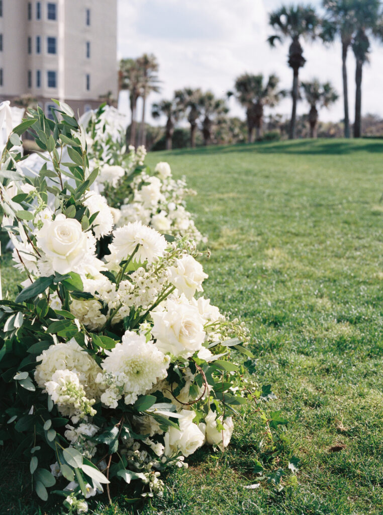 Film photo of monochromatic white floral arrangement at base of aisle for wedding ceremony. 