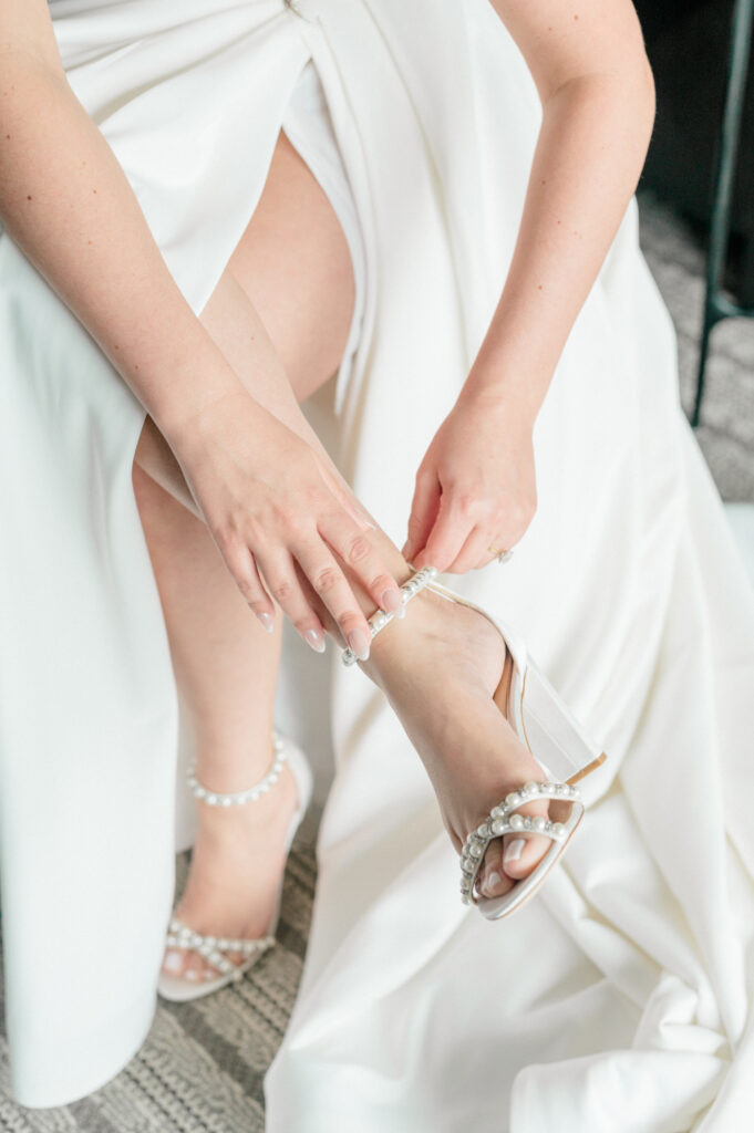 Bride finishing getting ready by buckling the anklet of her pearl heels. 