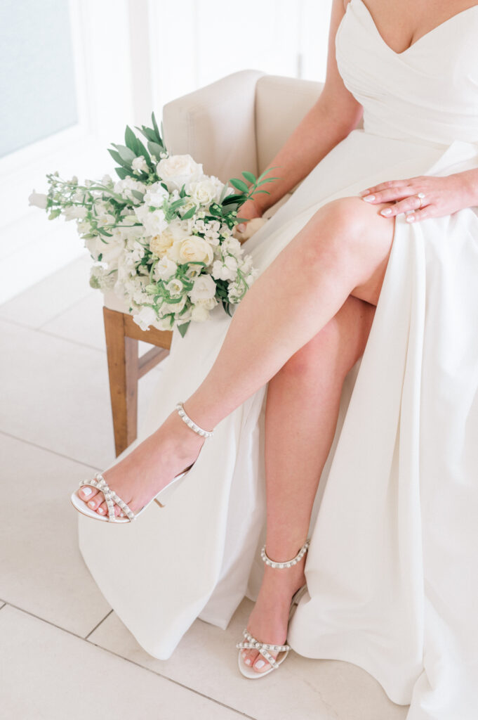 Bride sits with her leg crossed and bouquet in hand as her wedding photographer takes bridal portraits.