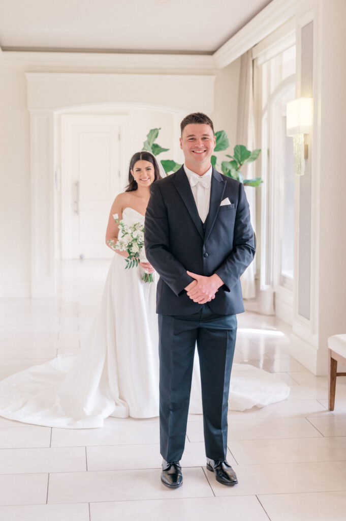 Bride stands behind groom before first look. 