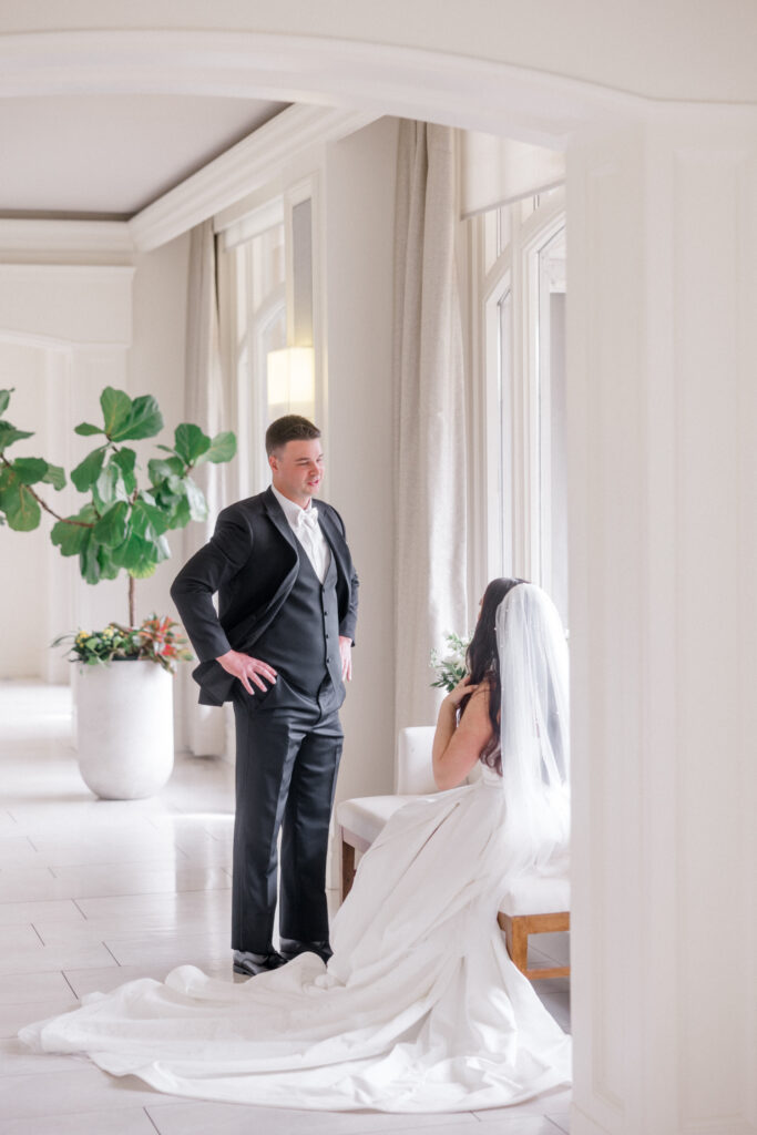 Groom stands and chats with bride, sitting, in their getting ready suite shortly before wedding ceremony. 