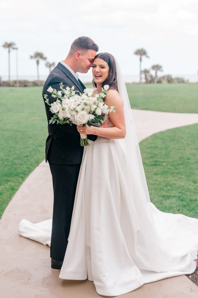 Bride and groom smiling and embracing as the bride laughs and holds monochromatic bouquet. 