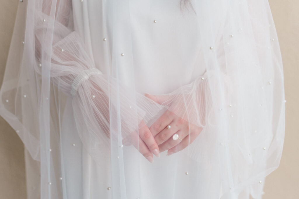 Detail shot of bride's ring and veil draped over her. 