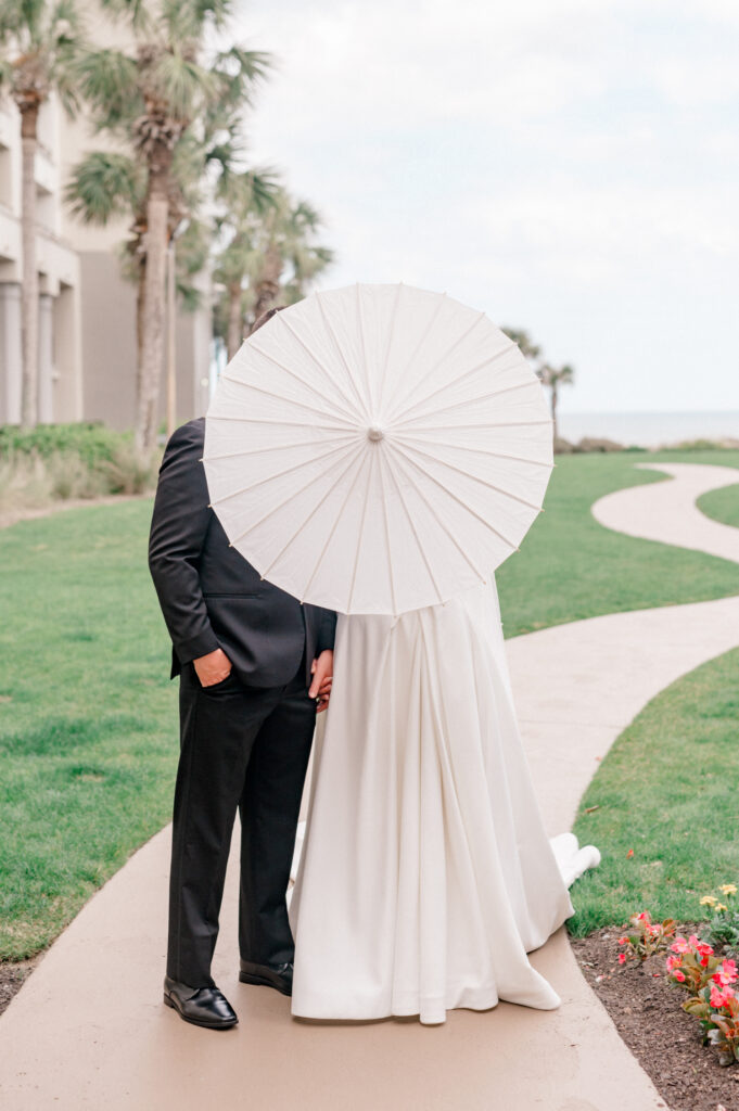 Bride and groom posing behind white umbrella. 