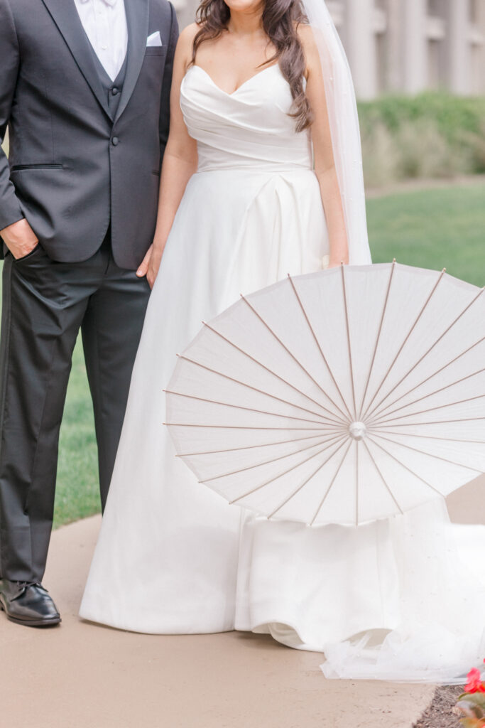 Bride and groom standing and holding white umbrella. 