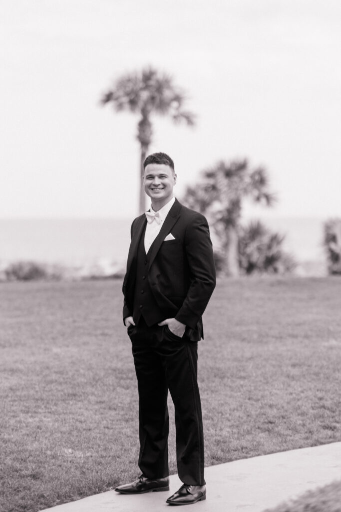 Black and white photo of groom standing on sidewalk of courtyard at the Ritz Carlton Amelia Island. 