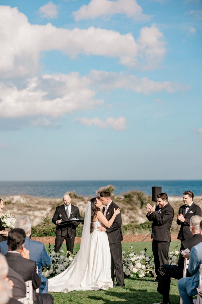 Bride and groom share first kiss after wedding at the Ritz Carlton Amelia Island with a stunning view of the dunes and Atlantic ocean behind them. 