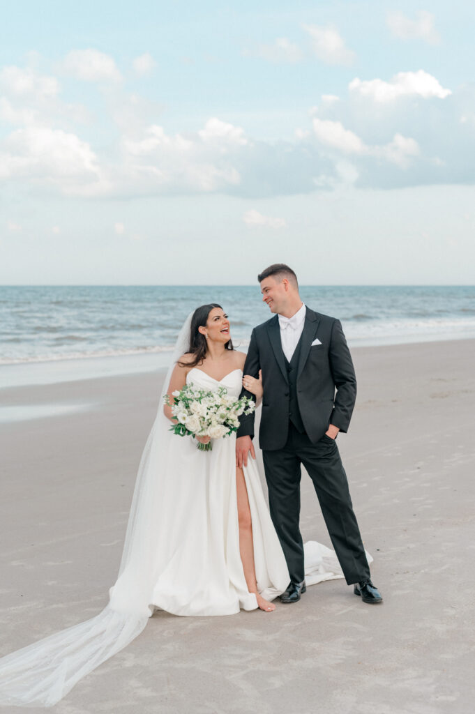 Bride and groom walk together on the beach, looking into each others eyes. 