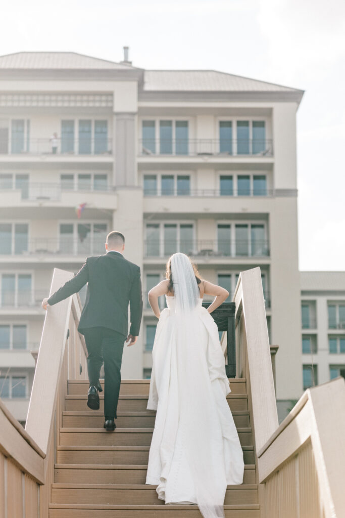 Bride and groom exiting ceremony walking up beach stairs together as they head towards their reception. 