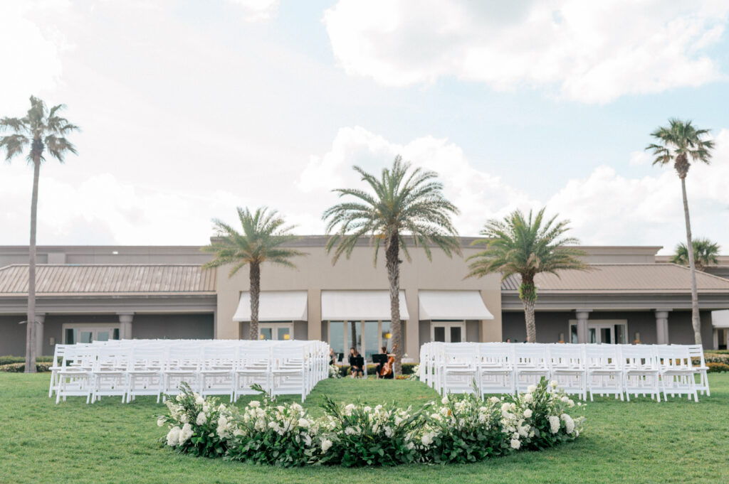 View of ground-level floral arch with white folding chairs set for wedding ceremony. 