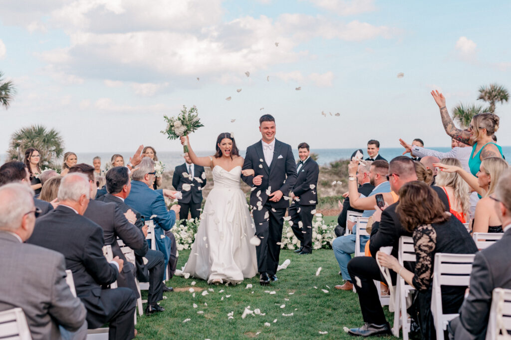 Recessional of bride and groom as white flower petals are being tossed by guests. 