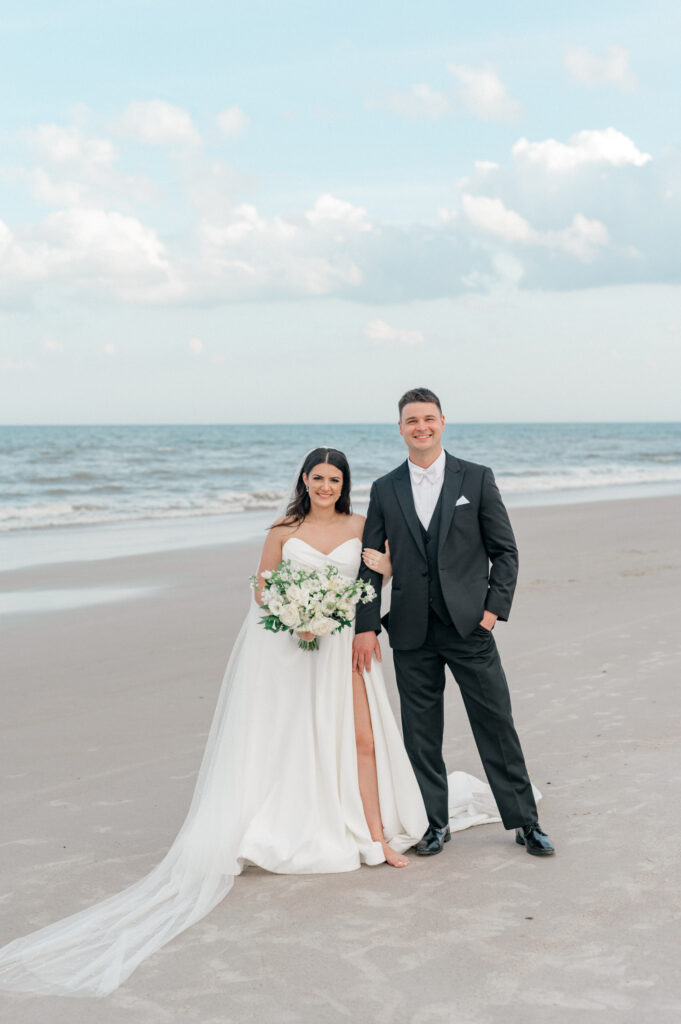 Bride and groom stand together on the beach with the Atlantic ocean behind them. 