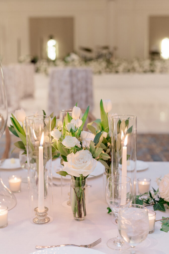 Bud vase of white florals and greenery surrounded by taper candles. 