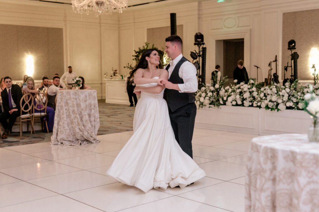 Bride and groom share first dance together on white tile dance floor. 