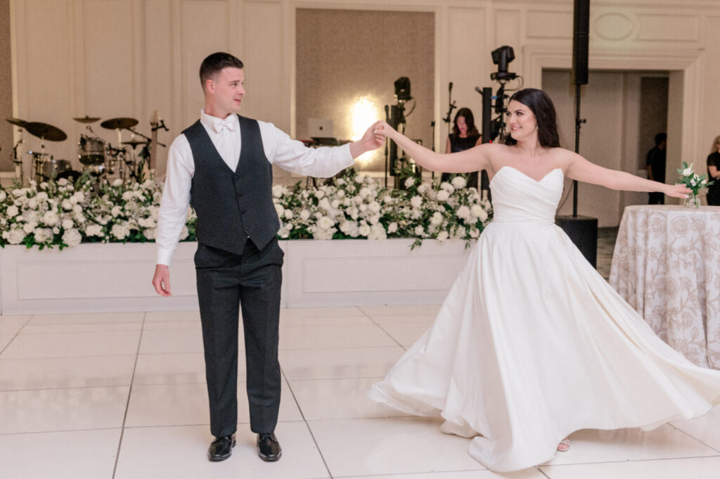 Bride and groom share first dance together on white tile dance floor. 