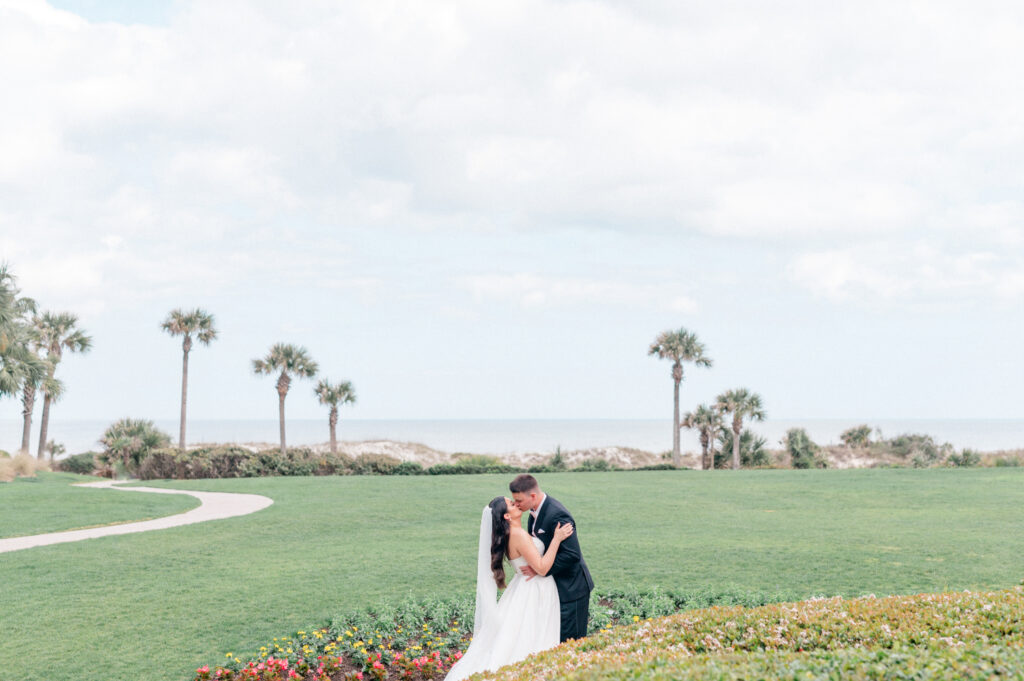 Bride and groom kiss on lawn of the Ritz Carlton Amelia with a beautiful ocean and palm tree backdrop. 