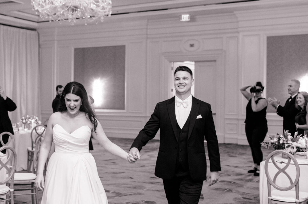 Black and white photo of bride and groom making their way to the dance floor. 