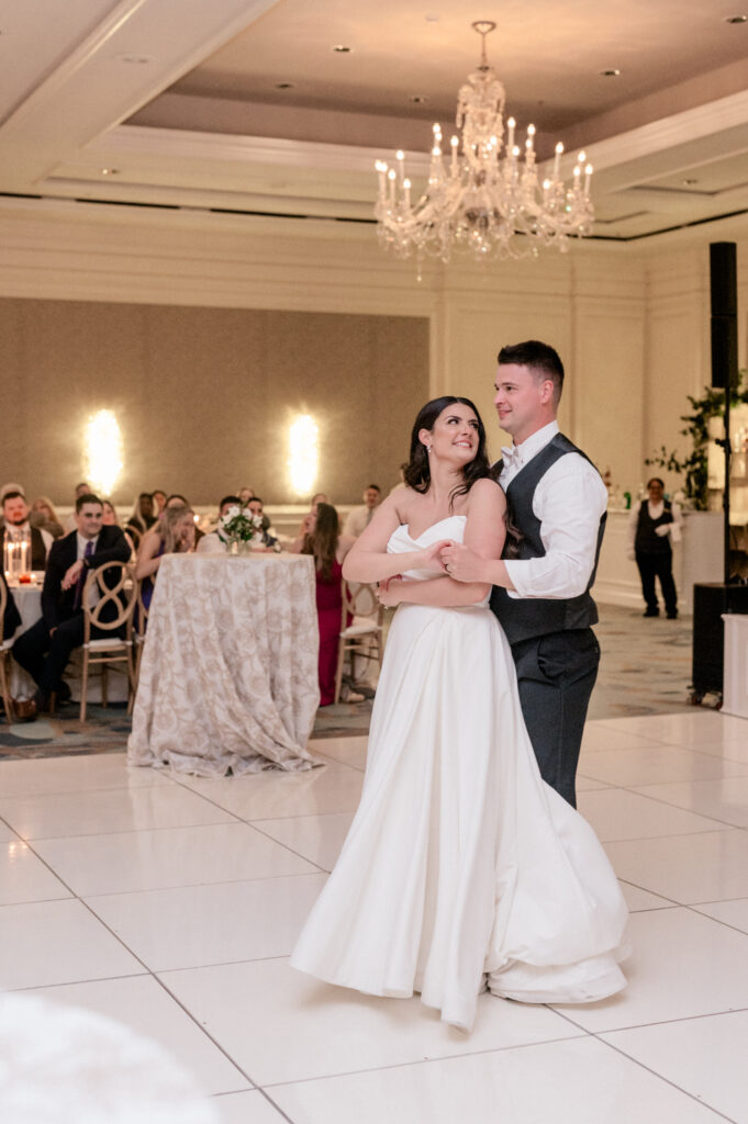 Bride and groom share first dance together on white tile dance floor. 