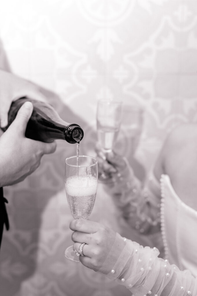 Black and white close up photo of groom pouring champagne into glass. 