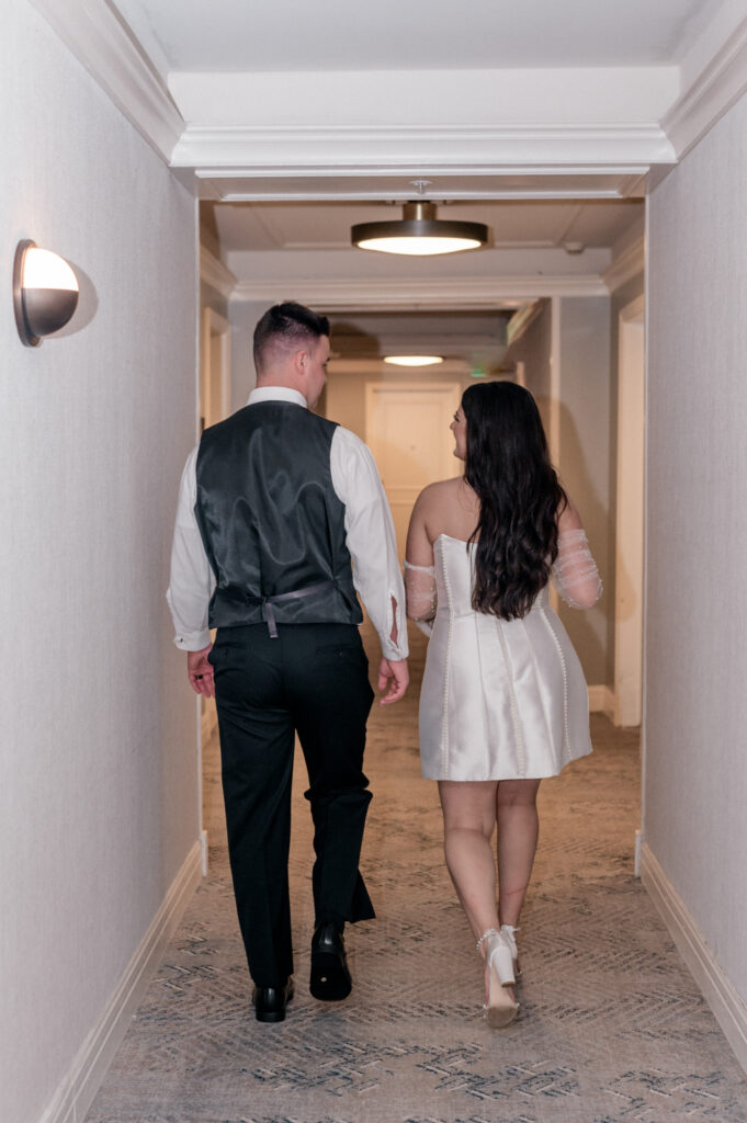 Bride and groom walk together in hallway of hotel. 