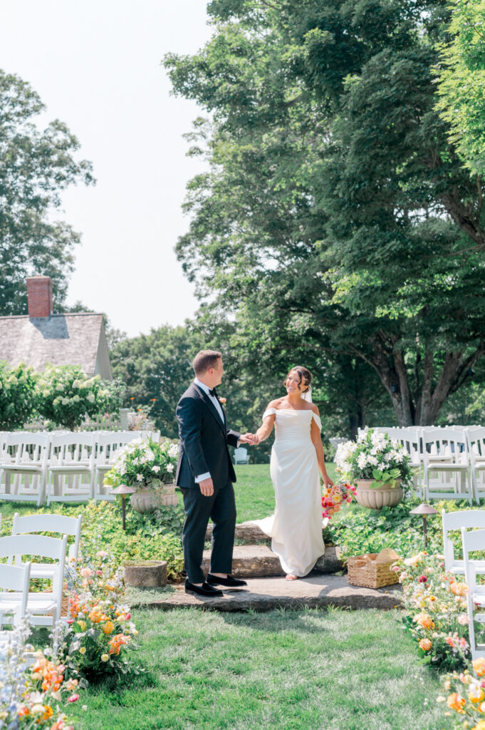 Bride and groom walk hand-in-hand down the floral-lined ceremony aisle at Smith Farm Gardens.