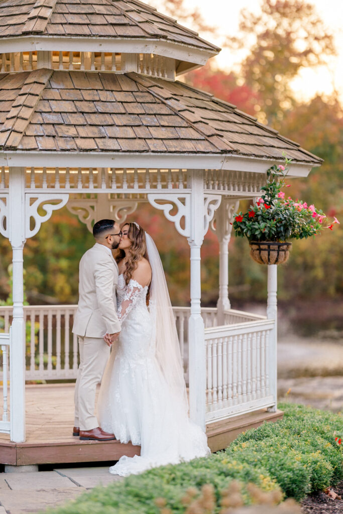 Bride and groom share a kiss under a charming white gazebo. 