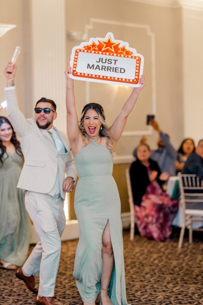 An ecstactic bridesmaid and groomsman raise a "Just Married" sign high as they make grand entrance into the reception. 