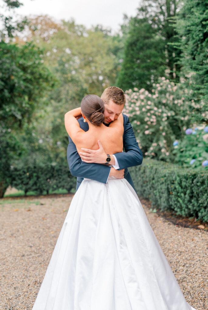 A bride and groom hug in a lush garden setting after their first look.