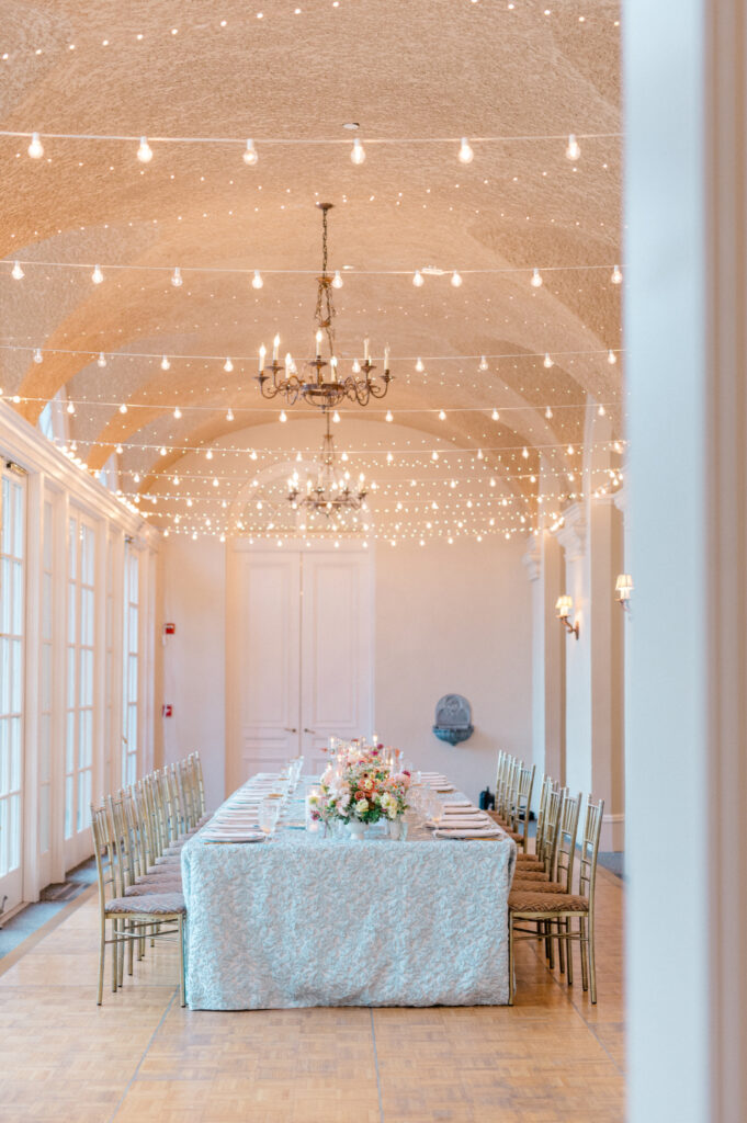 A reception table inside Wadsworth Mansion, set with floral centerpieces, soft linens, and twinkling lights strung from the ceiling. 