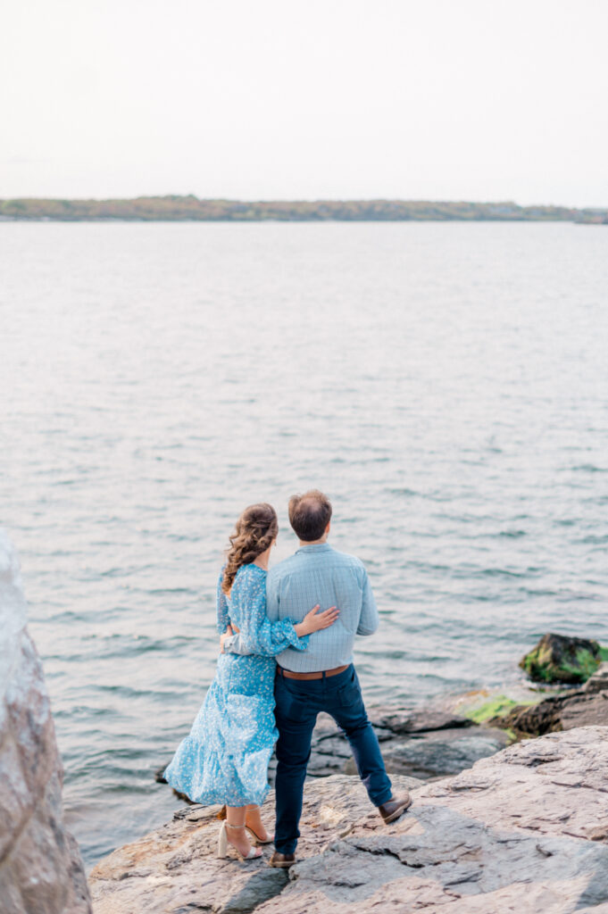 couple standing on the rocks overlooking the water during their engagement photos 