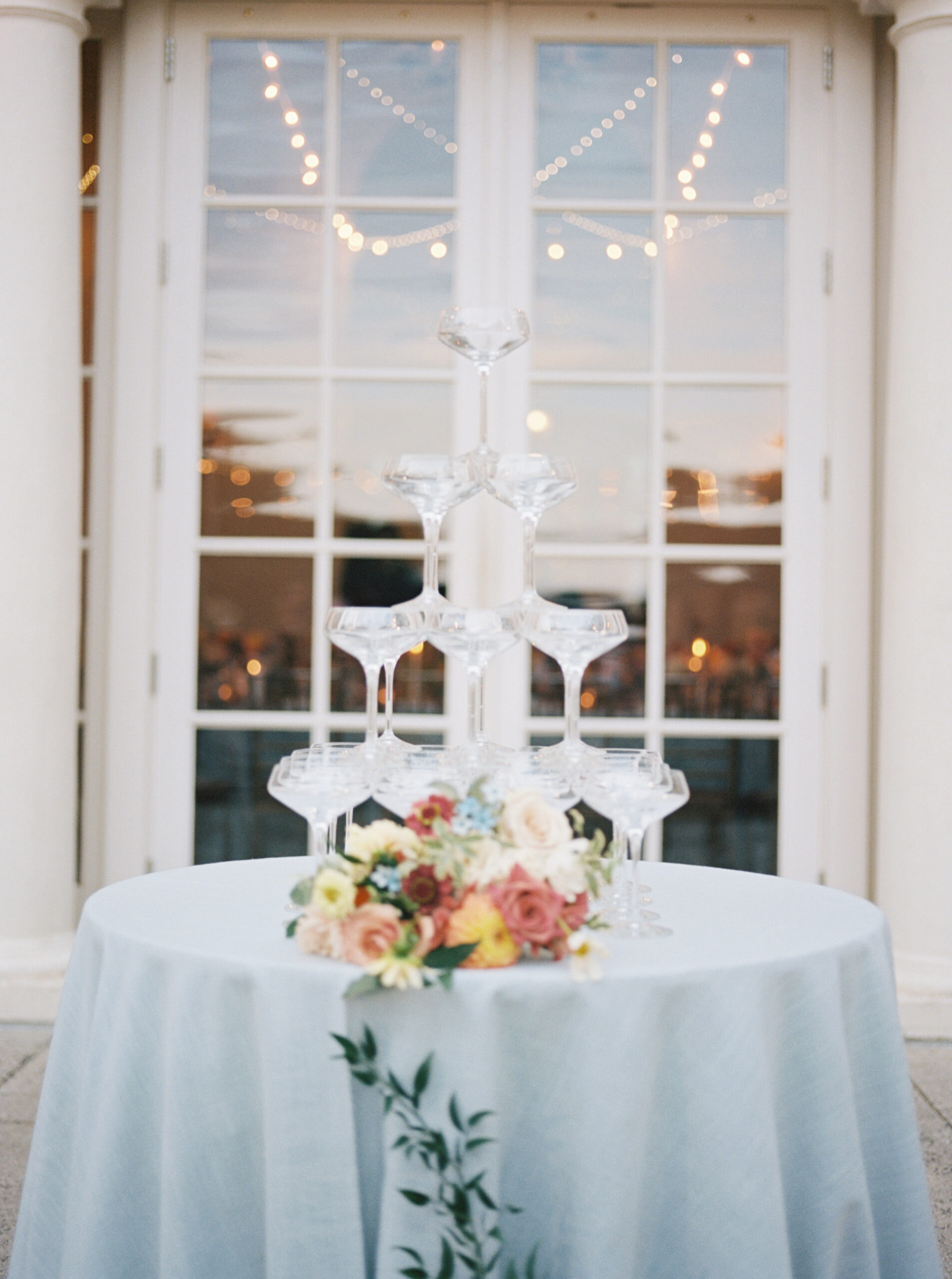 filled champagne glasses stacked on a white tablecloth with a floral bouquet in front