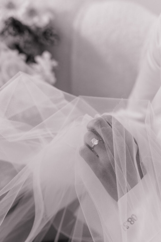 Black and white photo of bride's engagement ring peeking out from behind her veil 