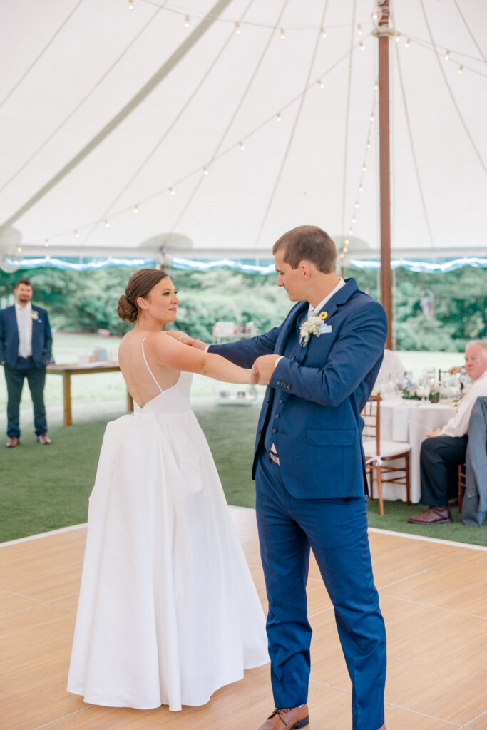 Bride and groom face each other during a twirl, mid-choreography, as they perform their first dance in a sunlit tent.