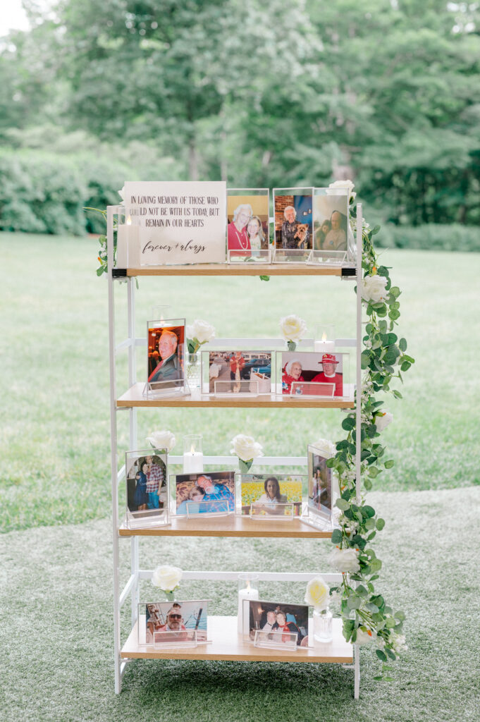 A remembrance shelf honoring loved ones with framed photos, white roses, and candles, displayed during Alexis and Doug’s elegant garden wedding.