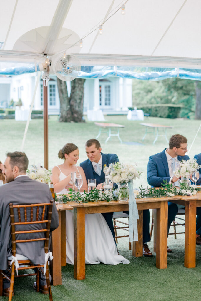 Alexis and Doug enjoying a quiet moment at their romantic reception table under the sailcloth tent, surrounded by soft blue and white florals.