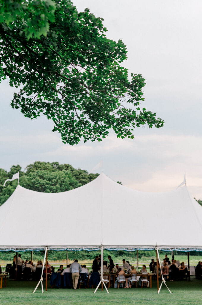 A classic white sailcloth tent surrounded by green fields and trees, setting the scene for a romantic New England wedding.