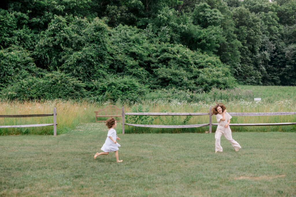 Candid wedding photo of children running barefoot through a field during cocktail hour at Smith Farm Gardens, showcasing natural joy and movement.