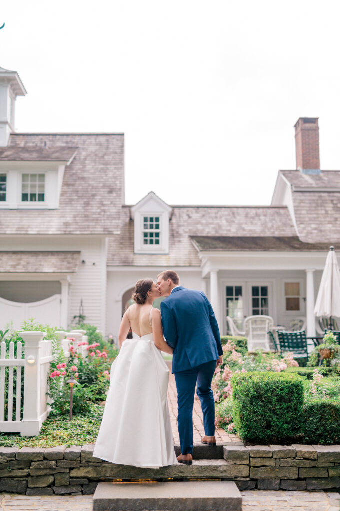 Romantic wedding portrait of couple kissing on stone steps with cottage-style backdrop at Smith Farm Gardens in Connecticut.