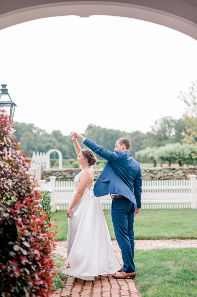 Bride and groom twirling beneath a white archway at Smith Farm Gardens, surrounded by white fences and lush garden paths.