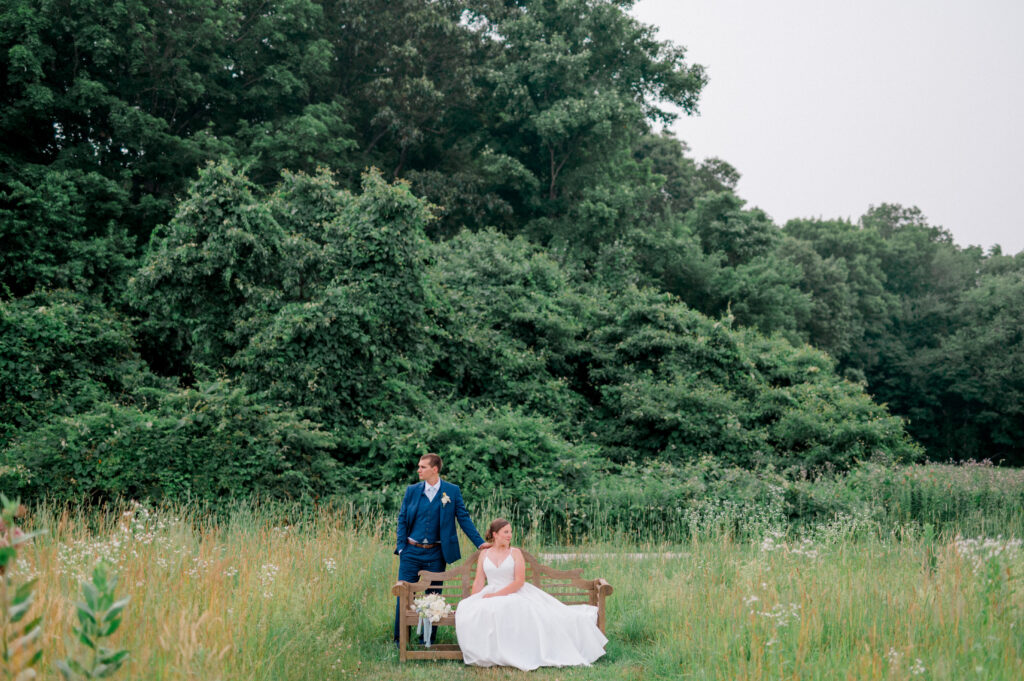 Alexis and Doug pose for a romantic portrait in a natural meadow at Smith Farm Gardens, surrounded by tall grass and lush greenery, creating a timeless and serene scene.