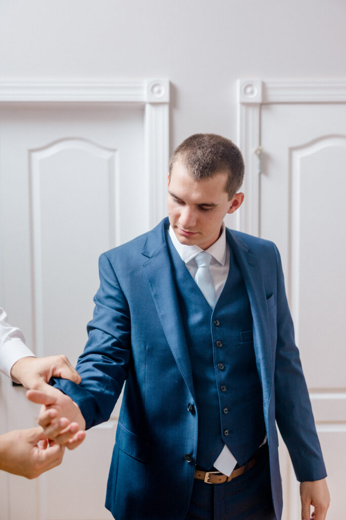 Groom receives help adjusting his sleeve cuffs, surrounded by groomsmen while getting dressed for his Smith Farm Gardens wedding.