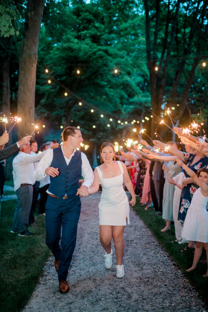 Alexis and Doug run hand-in-hand down a tree-lined path surrounded by guests holding sparklers during their grand exit at Smith Farm Gardens.