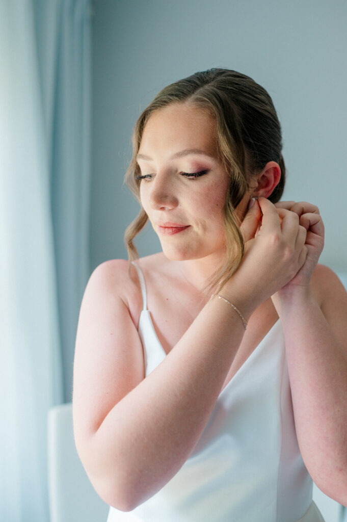 Bride putting on earrings by a soft-lit window, captured during her peaceful getting ready moment before her Smith Farm Gardens wedding.