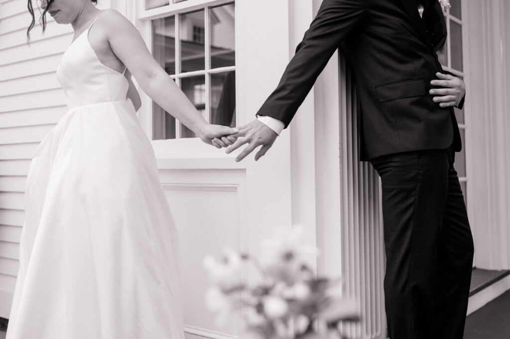 Bride and groom holding hands around corner during first touch at Smith Farm Gardens wedding