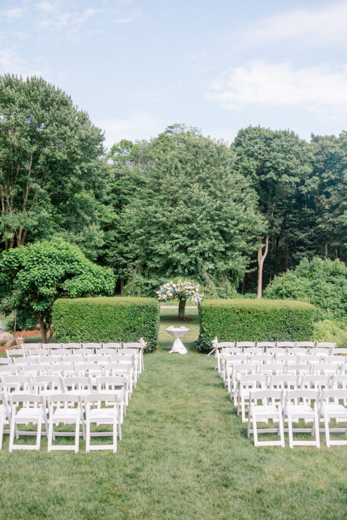Outdoor garden ceremony setup at Smith Farm Gardens, featuring rows of white chairs and a lush floral arbor framed by greenery.